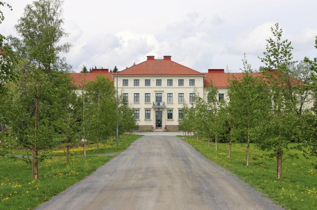 un camino vacío frente a un edificio blanco con techo rojo en Hostel Bjorkenheim en Seinäjoki