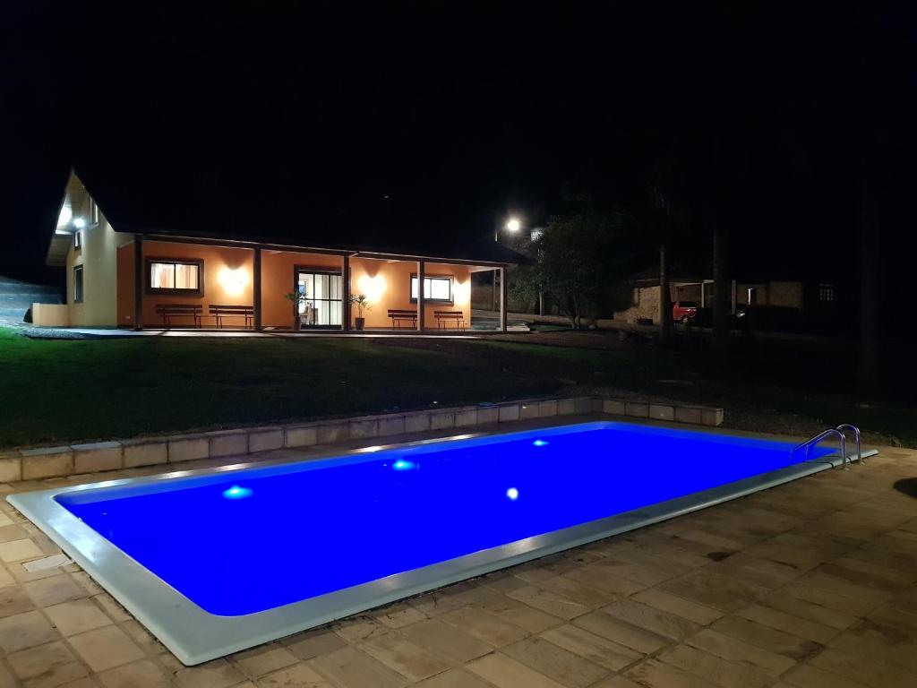 a blue swimming pool in front of a house at night at Cabana Rústica - Sitio Kayalami in Tijucas do Sul