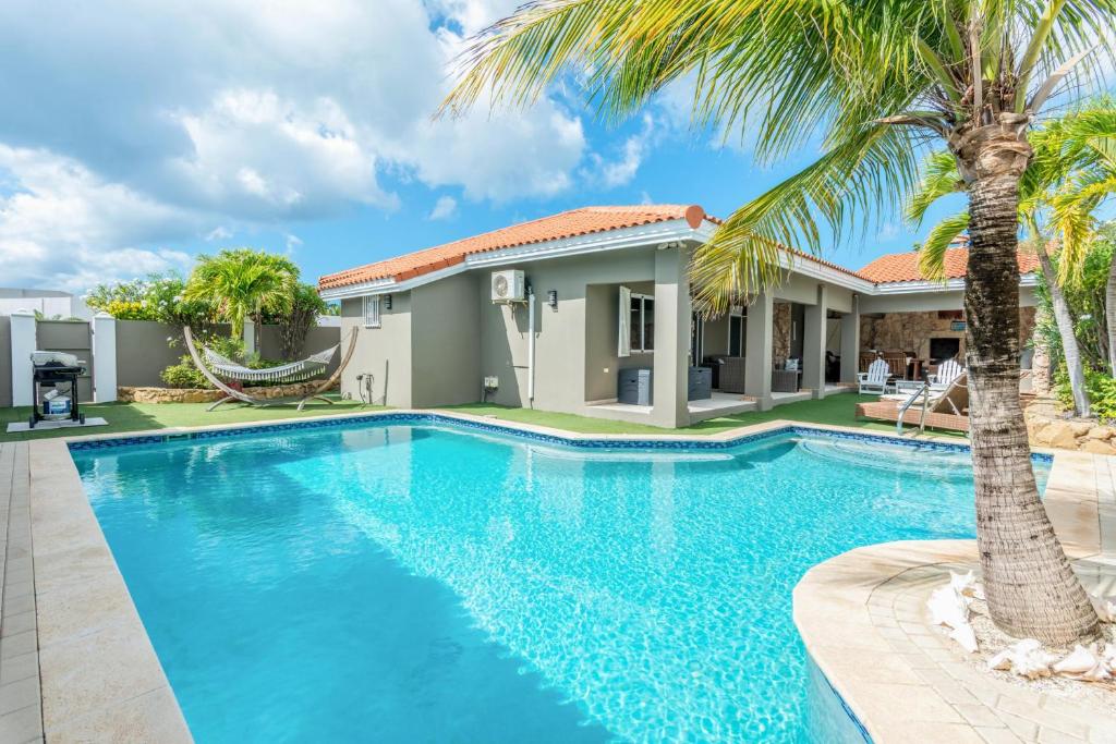 a swimming pool in front of a house with a palm tree at Casa Karlina in Palm-Eagle Beach