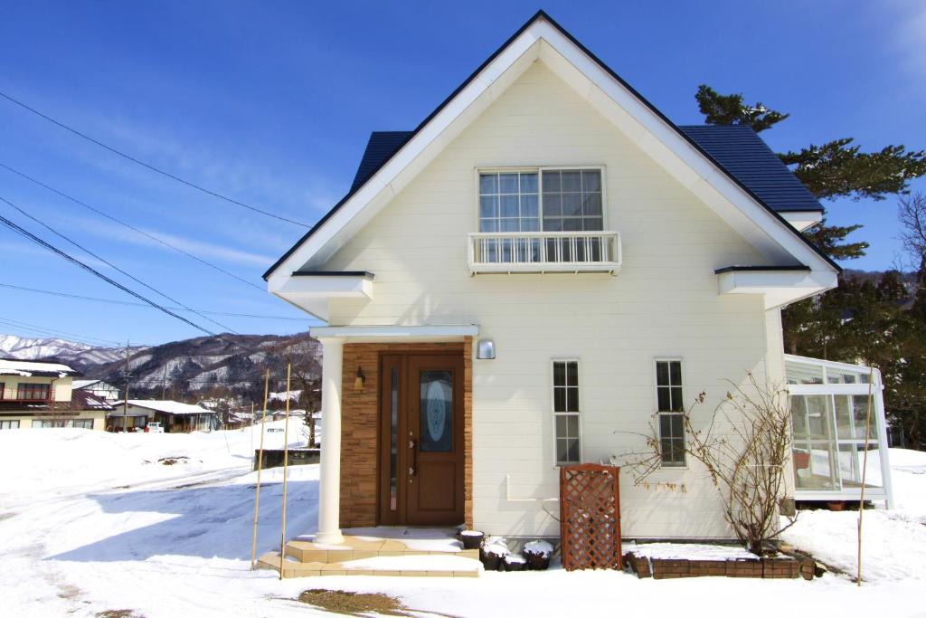 a white house with a wooden door in the snow at Hakuba Mountain Chalet in Hakuba
