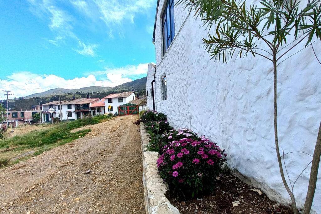 a white building with flowers next to a dirt road at Posada Villa Sarita in Monguí