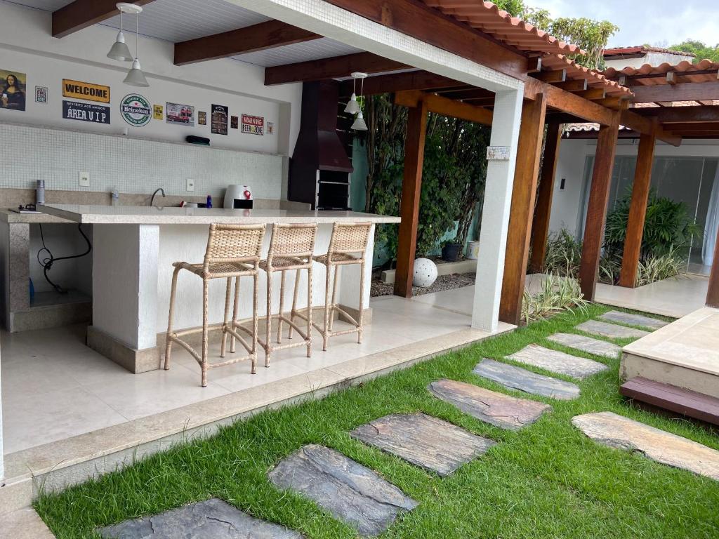 a patio with a bar with stools in the grass at Casa da Jana com piscina in Porto Seguro