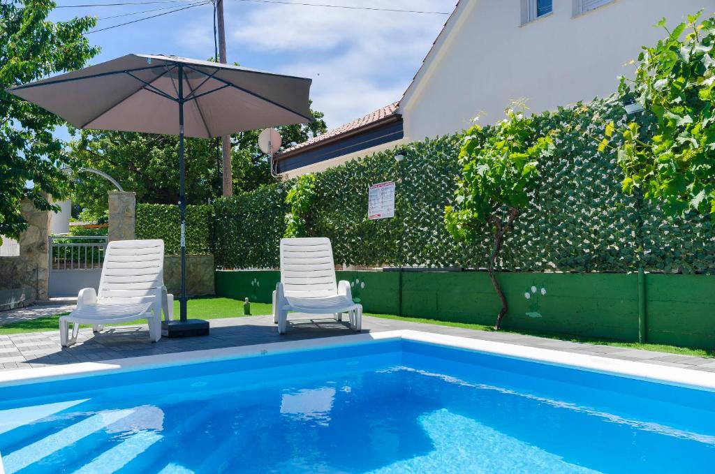 zwei Stühle und ein Sonnenschirm neben einem Swimmingpool in der Unterkunft Apartment Milena in Srima