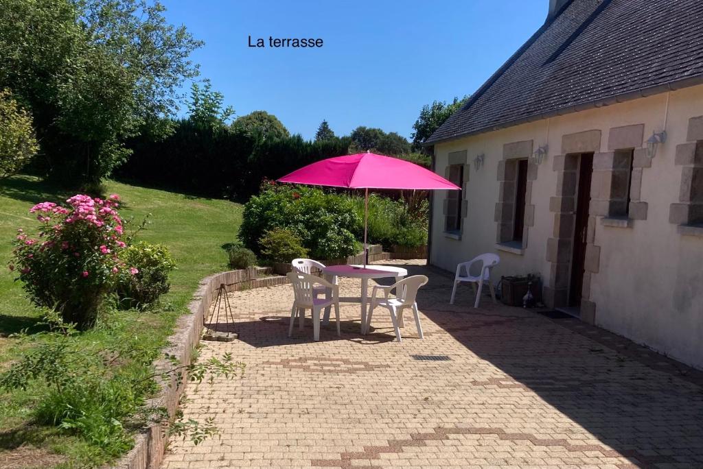 a table and chairs with a pink umbrella in a yard at Maison de campagne de plein pied. in Plougonven