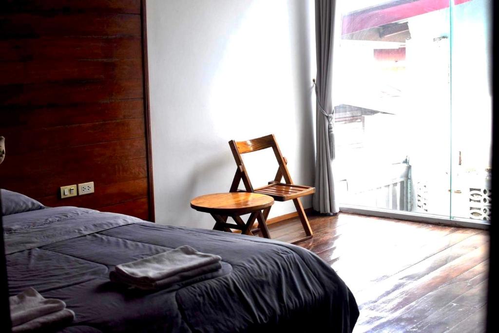 a bedroom with a bed and a chair and a window at Une Jai Place เรือนอุ่นใจ in Phimai