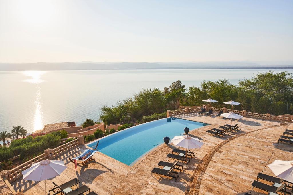 een uitzicht over een zwembad met stoelen en parasols bij Mövenpick Resort & Spa Dead Sea in Sowayma