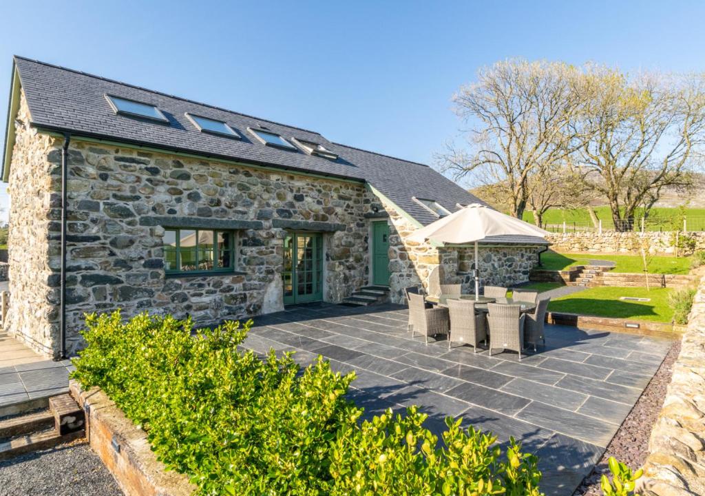 a stone cottage with a patio and umbrella at Bwthyn Nant Bach in Dolbenmaen
