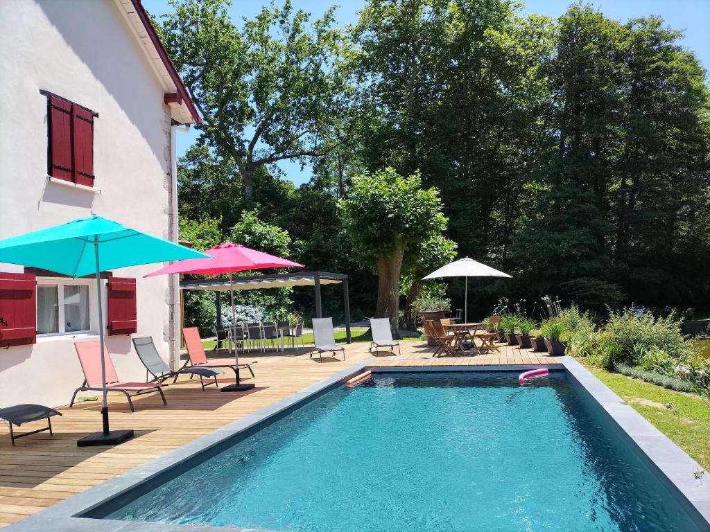 a swimming pool with chairs and umbrellas next to a house at Le Moulin de Saubrigues in Saubrigues