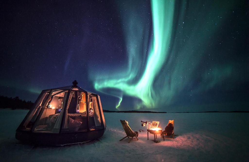 a tent and chairs in the snow under the northern lights at Aurora hut igloo in Rovaniemi