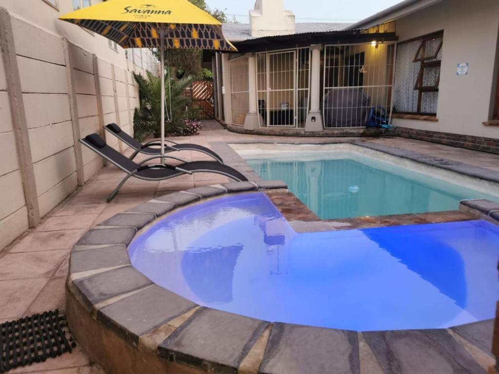 a swimming pool with an umbrella next to a house at Cammy's Guesthouse in Kuilsrivier