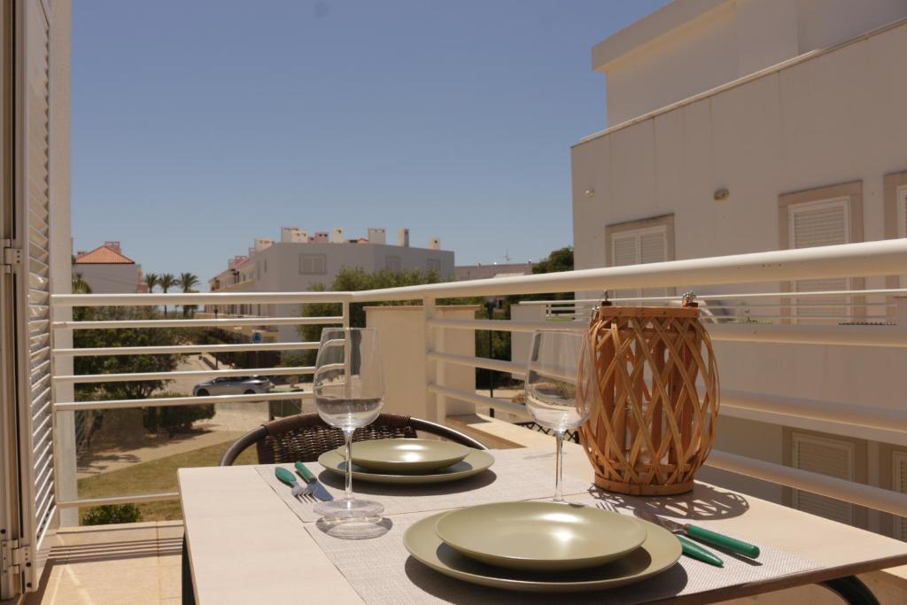 a table with plates and wine glasses on a balcony at Apartamento Formosa Mar by YHA in Cabanas de Tavira