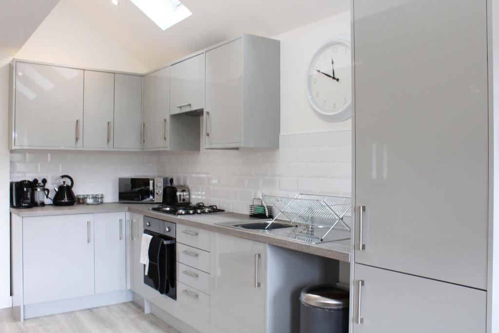 una cocina con armarios blancos y un reloj en la pared en Abingdon - Private Flat with Garden & Parking 10 en Abingdon