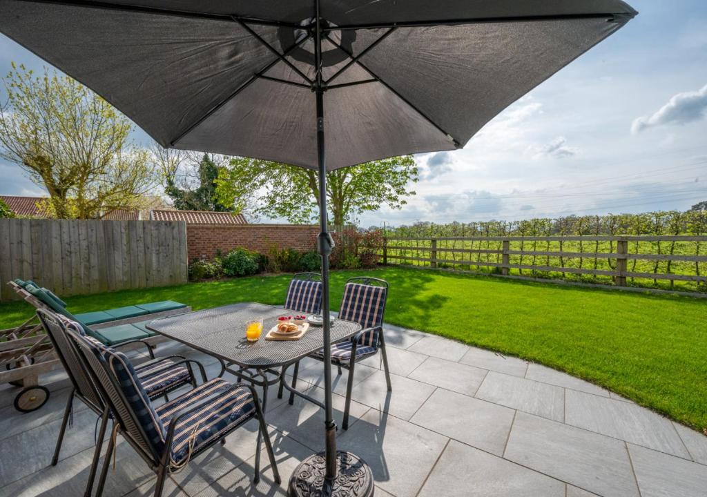 un patio con mesa, sillas y sombrilla en Beech Corner en Cawston