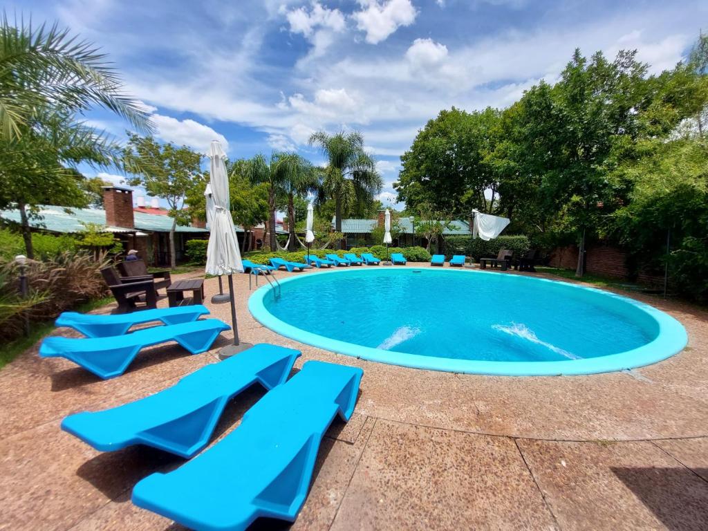 uma piscina com cadeiras azuis e guarda-sóis em Hotel Jardines de Dayman em Termas del Daymán