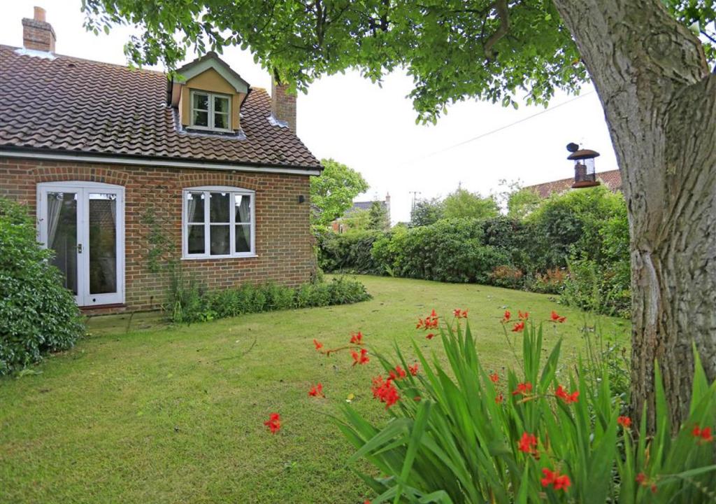 uma casa de tijolos com um quintal com flores vermelhas em 1 Chequers Row em Friston