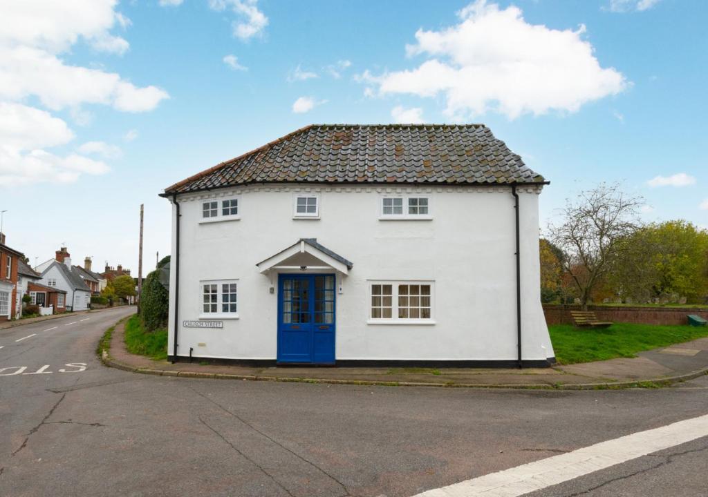 uma casa branca com uma porta azul numa rua em Corner Cottage em Wangford