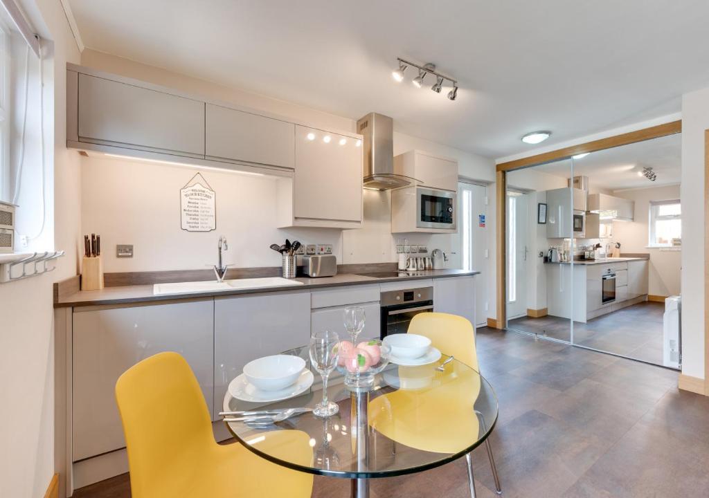 a kitchen with a glass table and yellow chairs at The Harnser in Beccles