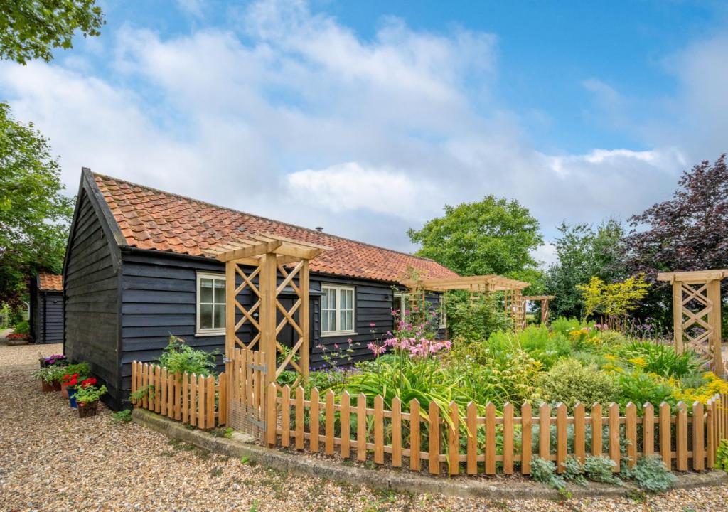 une petite maison noire avec une clôture en bois dans l'établissement Woodland Lodge, à Wilby