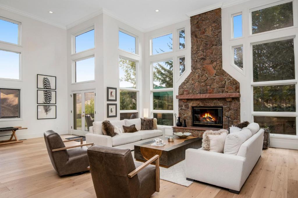 a living room with white furniture and a stone fireplace at Modern Beaver Creek Private House! in Avon