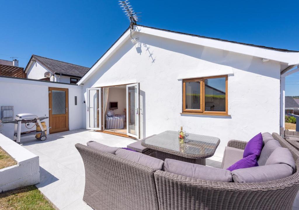 a patio with wicker chairs and a table and a house at 73 Cae Du in Abersoch