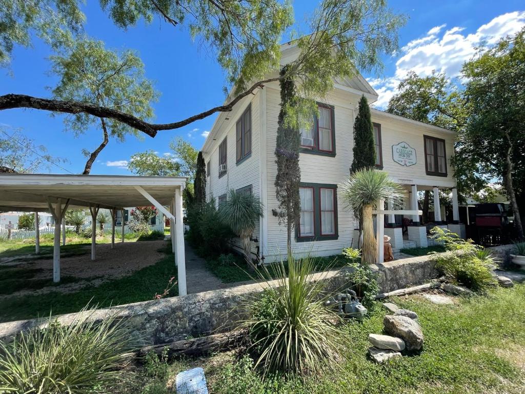 a white house with a porch and trees at Carriage Inn Bandera Suite 2 in Bandera