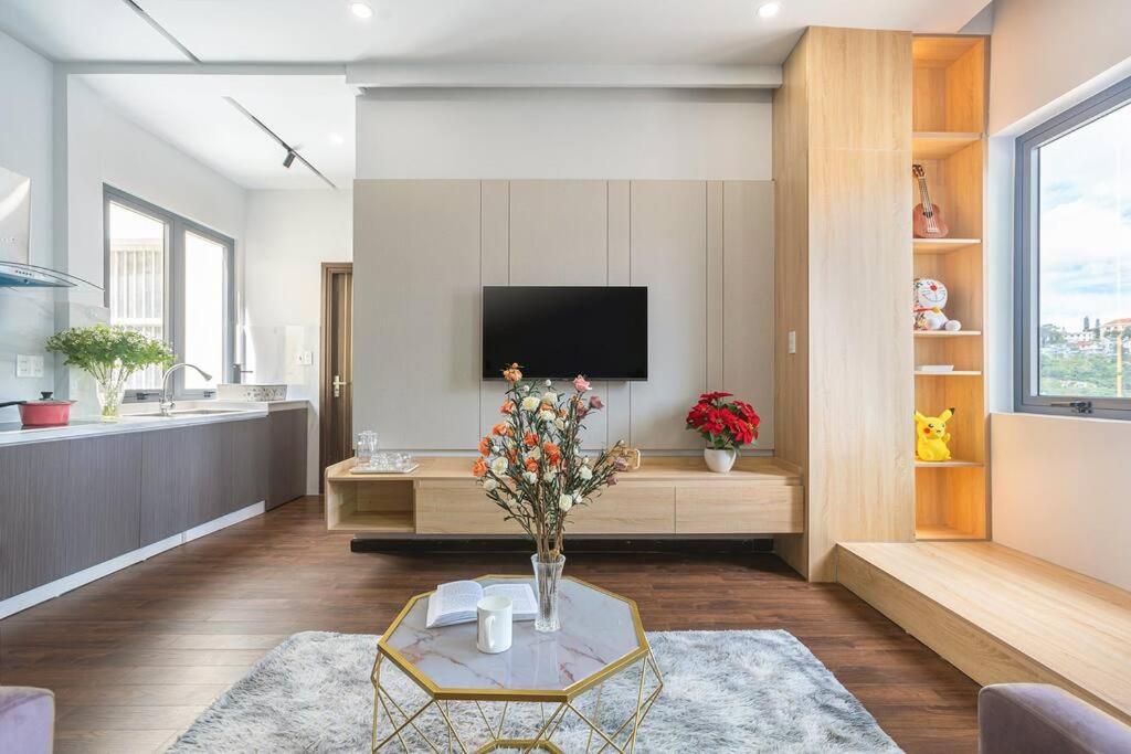 a living room with a television and a table with flowers at MCK Homestay Da Lat-Can Ho 208 in Ấp Ða Lợi
