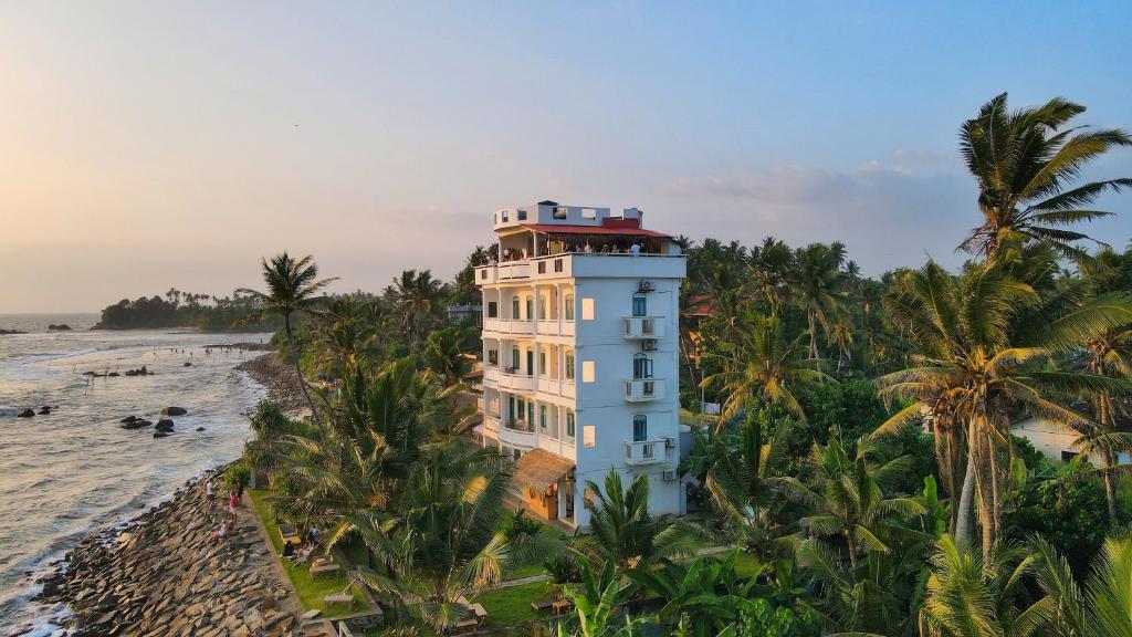 a building on the beach with palm trees at Lighthouse Ahangama in Ahangama