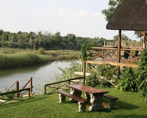 a picnic table next to a river with a hut at River Bank Lapa in Upington