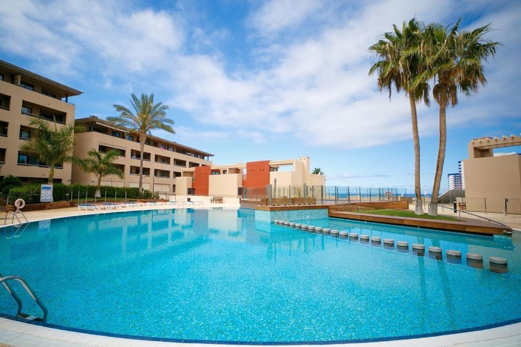 une grande piscine avec des palmiers et des bâtiments dans l'établissement Spacious and comfortable Paraiso II, à Playa Paraiso