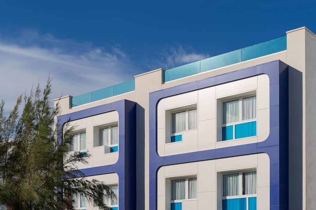 a white and blue building with a tree in front of it at Las Afortunadas , Playa Arinaga 1ºA in Arinaga