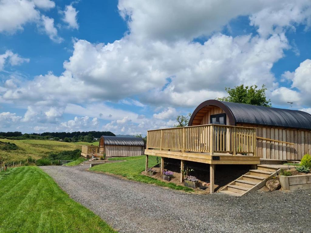 a barn with a deck and a house on a gravel road at Luxury Glamping Pods - The Heft & The Hirsel in Glasgow