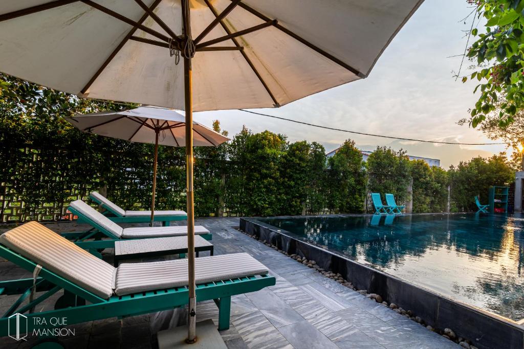 an umbrella and chairs next to a swimming pool at Tra Que Mansion in Hoi An