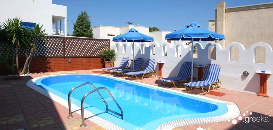 basen z niebieskimi leżakami i parasolami w obiekcie Pension Stella w mieście Karterados