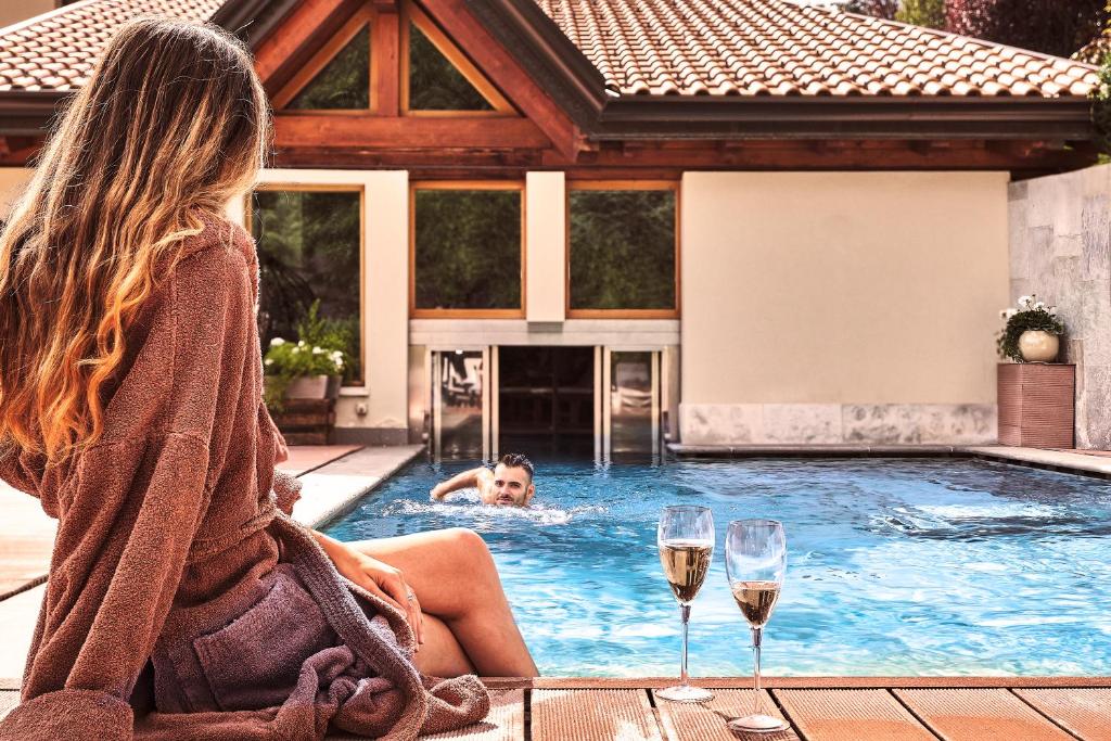 una mujer sentada en una piscina con copas de vino en Hotel Salvadori en Mezzana