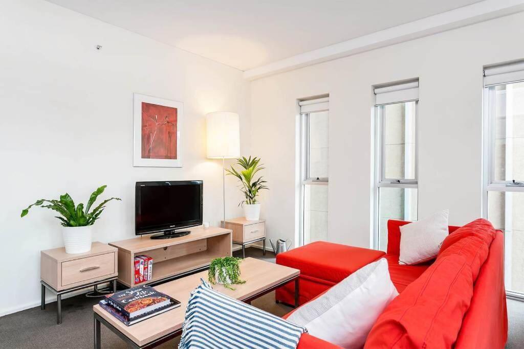a living room with a red couch and a tv at City Centre Apt - 3 Bed/Parking/CBD/WiFi in Adelaide