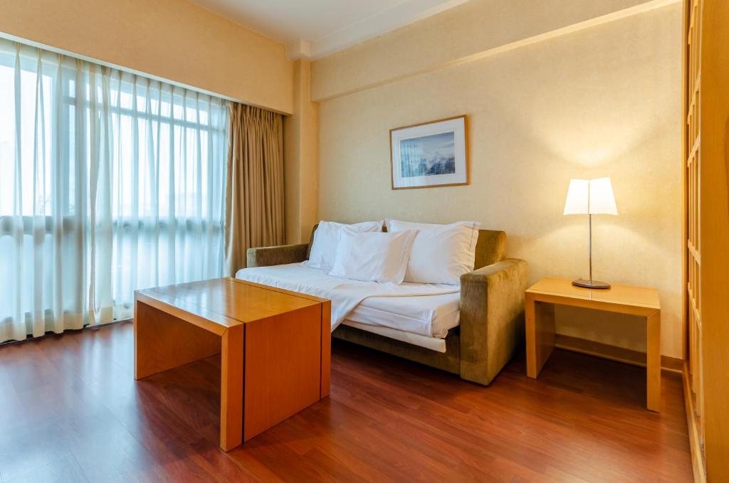 A bedroom with a double bed, wooden coffee table, armchairs and a large curtained window.