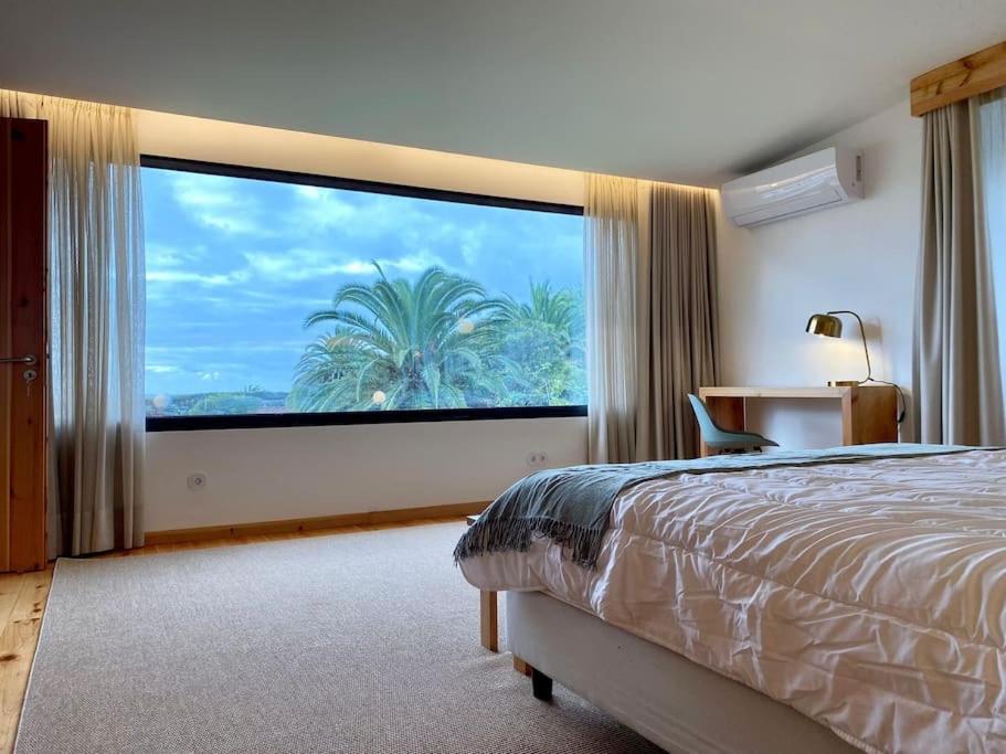 a bedroom with a large window with a palm tree at Nature & Sea - Casa Vinhateira West Duplex in Caloura