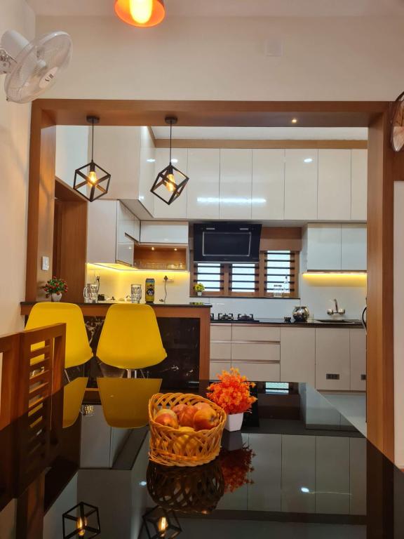 a kitchen with yellow chairs and a table with a basket of fruit at Milaano Orchids, Service Villa, Kammana Mananthavady in Wayanad