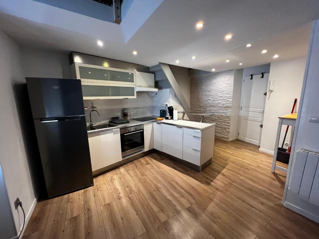 kuchnia z białymi szafkami i czarną lodówką w obiekcie NIMES Superbe appartement duplex climatisée w mieście Nîmes