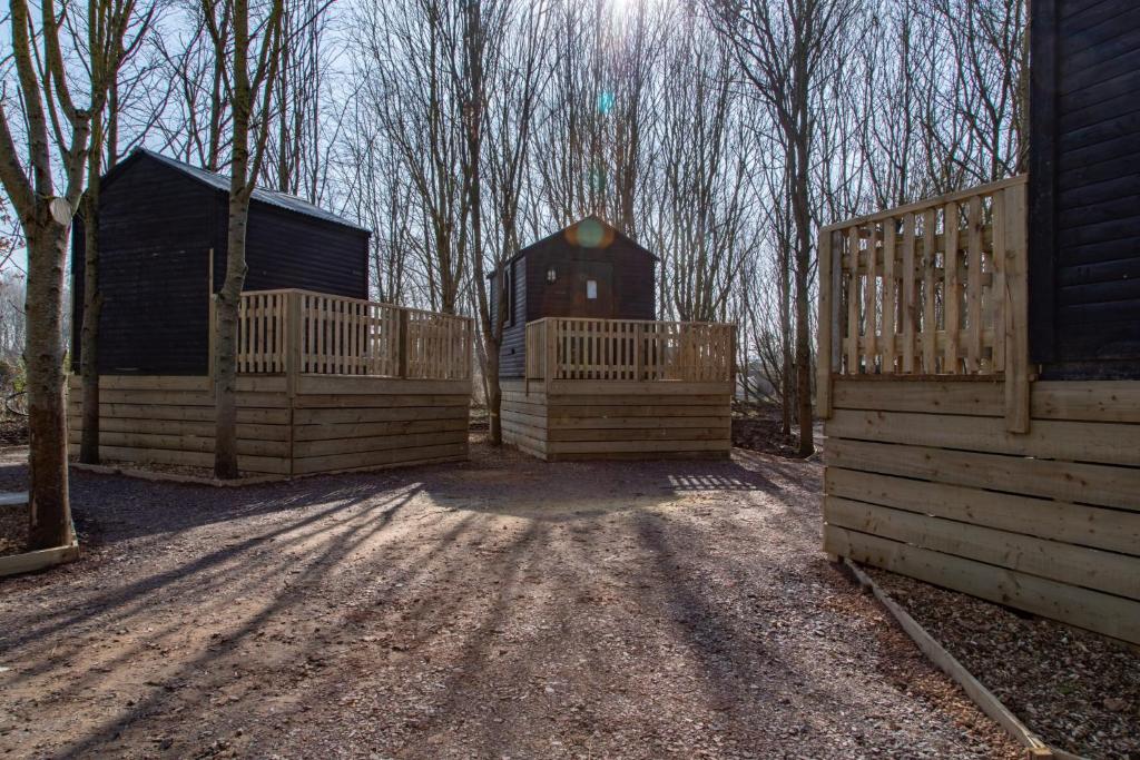 a wooden fence with a barn and trees in the background at Fairwood Lakes Holiday Park- Fishing Breaks - Woodland Huts in North Bradley
