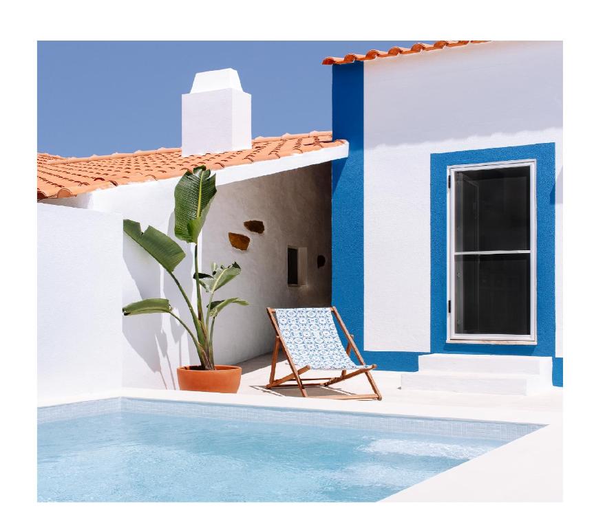 a blue and white house with a chair next to a pool at Quinta das Alfazemas in Ericeira