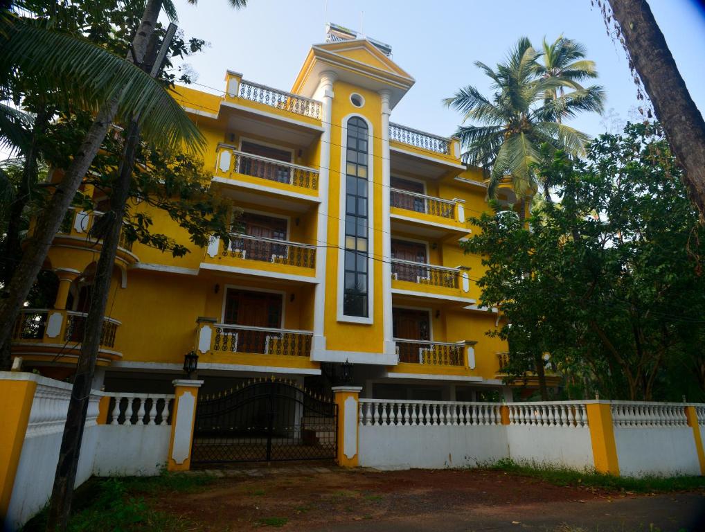 a yellow building with a white fence and palm trees at Antonio's Residency Goa in Betalbatim
