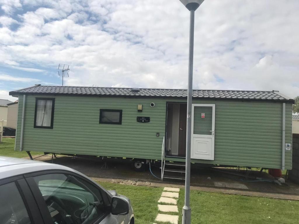 a green tiny house parked next to a car at Swift Loire (Field view 78) in Jaywick Sands