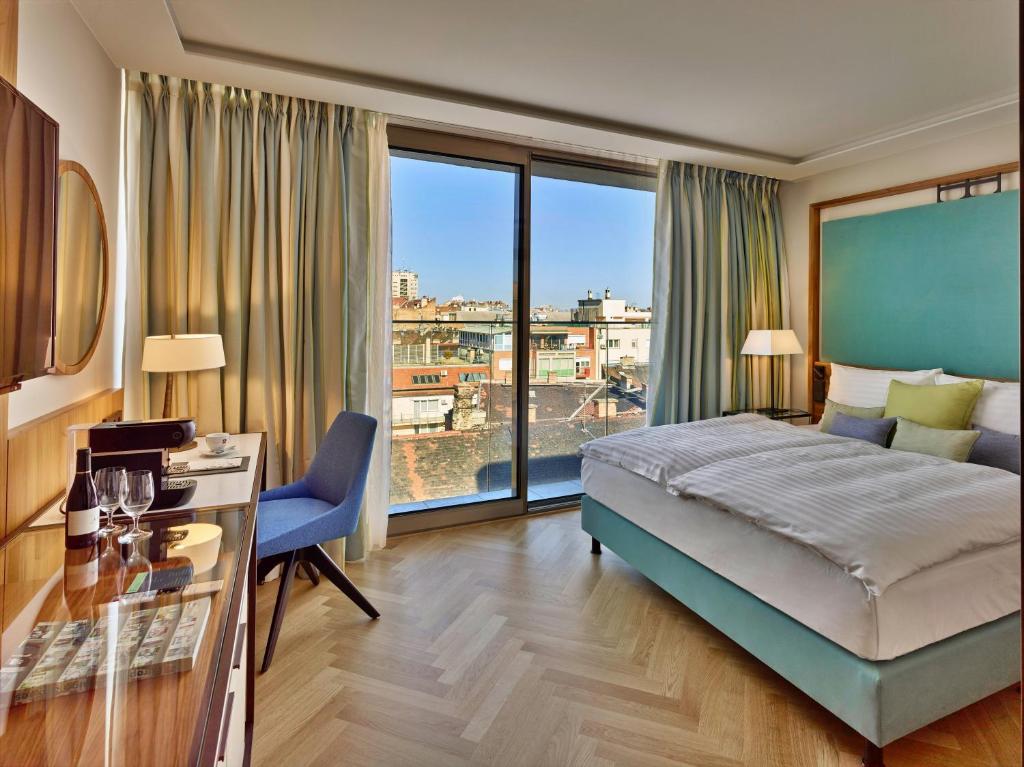 ブダペストにあるEST Grand Hotel Savoyのベッドと大きな窓が備わるホテルルームです。