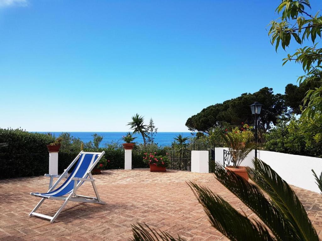 una silla azul sentada en un patio de ladrillo con el océano en el fondo en Villa del Sogno, en Parghelia