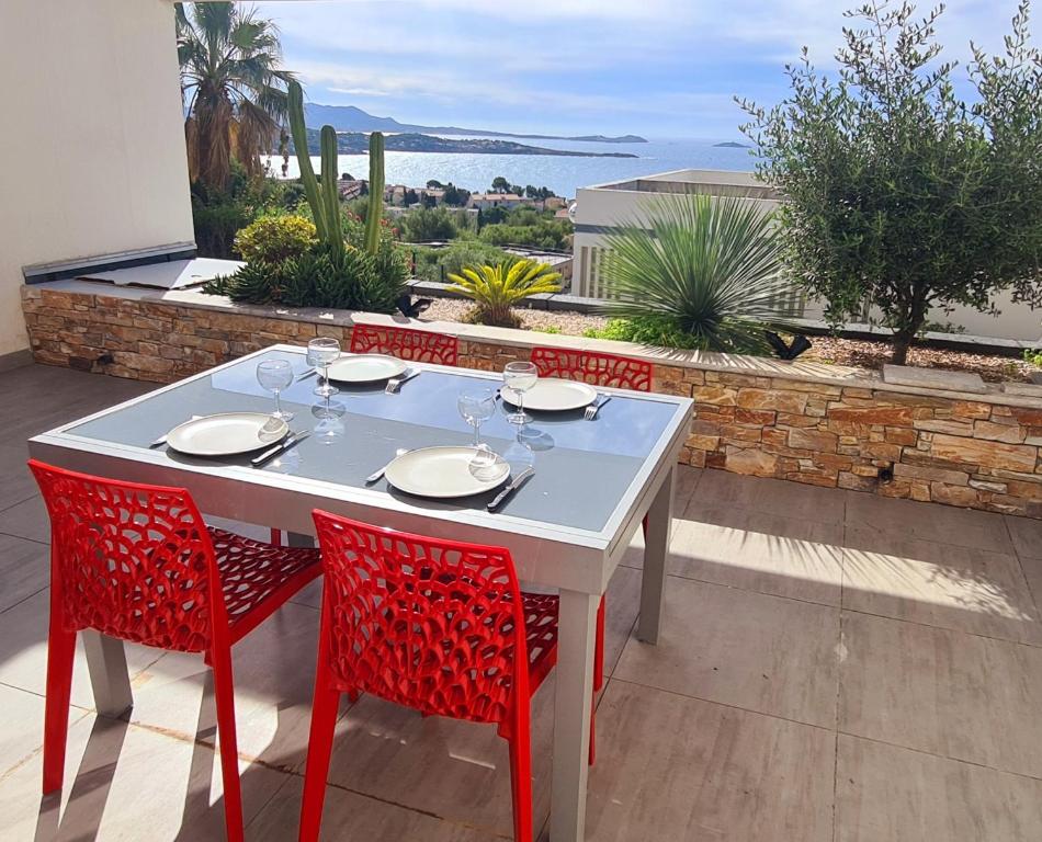 - une table avec des verres à vin et des chaises rouges sur la terrasse dans l'établissement MAGNIFIQUE APPARTEMENT VUE MER - GRANDE TERRASSE ET PISCINE, à Bandol