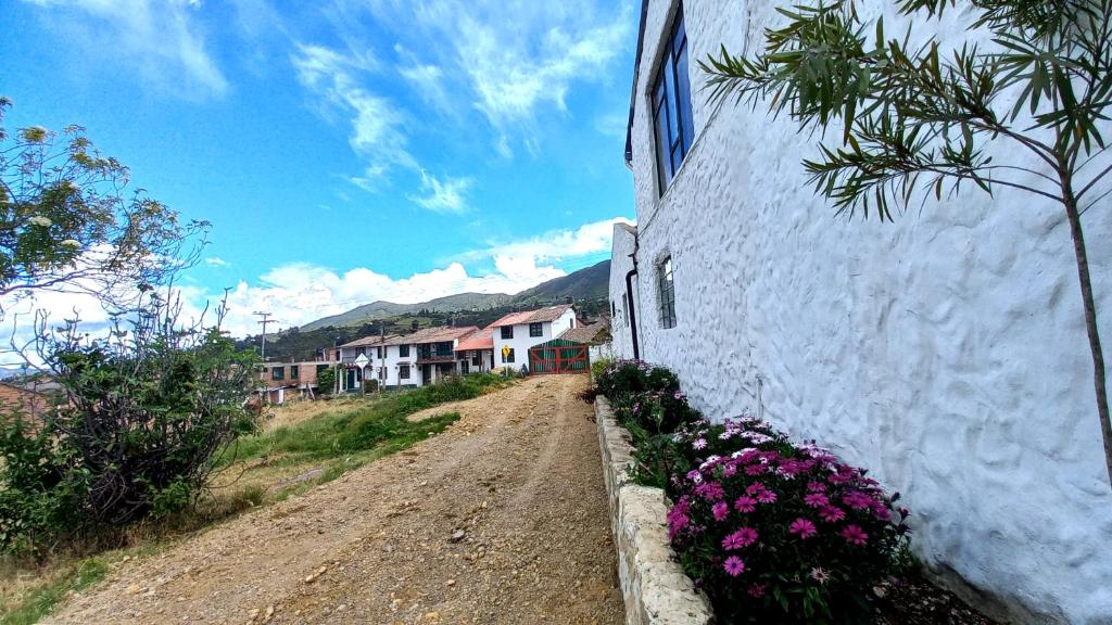 a dirt road next to a white building with flowers at Hospedaje y Camping del Rio in Monguí