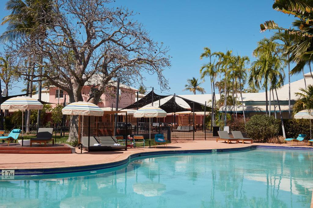 a swimming pool with chairs and umbrellas at The Continental Hotel in Broome