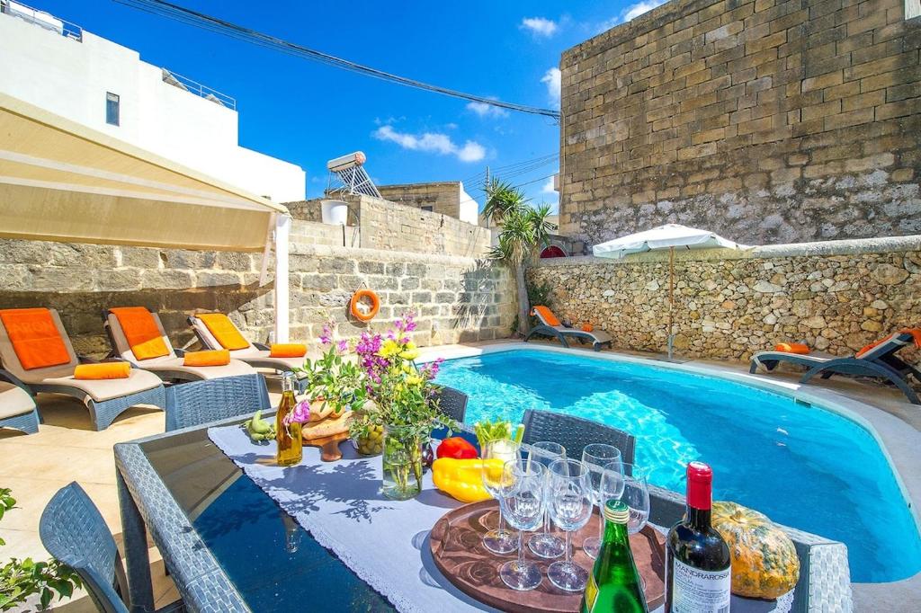 patio con tavolo, bicchieri da vino e piscina di Gawhra Holiday Home a Xagħra