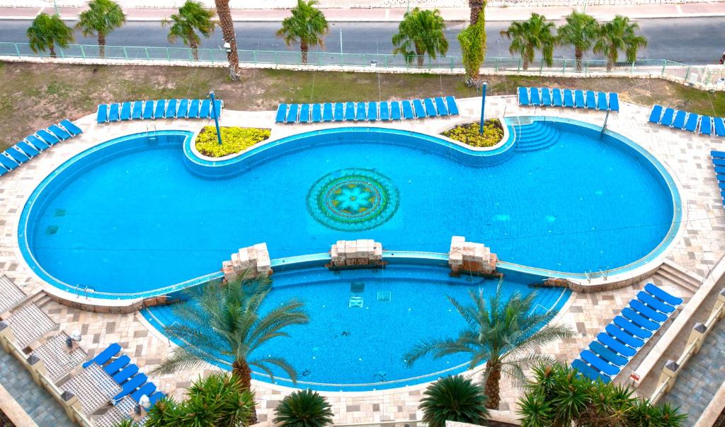 an overhead view of a large swimming pool with chairs and palm trees at Leonardo Plaza Hotel Dead Sea in Ein Bokek